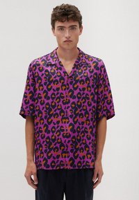 Camicia a maniche corte con bottoni di colore viola, caratterizzata da una stampa leopardata nera e arancione. Tessuto leggero con una vestibilità comoda e colletto.