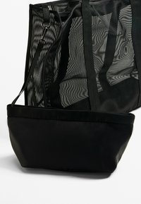 Black mesh tote bag with a solid black base. Features adjustable shoulder straps, a structural design, and a contrasting texture between materials.