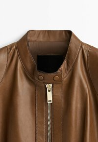 Brun läderjacka med ståkrage, guldzipper och tryckknappsstängning på en enkel vit bakgrund.