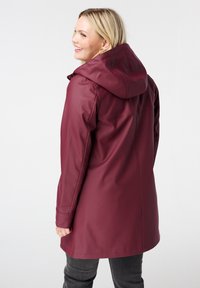 Veste imperméable bordeaux avec capuche, manches longues et texture lisse. Présente une coupe droite et un design minimaliste.