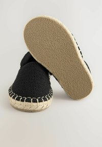 Schwarze Leinen-Espadrilles mit einer strukturierten Oberfläche, Jutenähten entlang der Sohle und einer gummierten beigen Außensohle für besseren Halt.