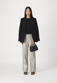 Μαύρο προσαρμοσμένο σακάκι, εφαρμοστό μαύρο τοπ, γυαλιστερά ασημί παντελόνια σε φαρδιά γραμμή με σχέδιο κροκοδείλου, μαύρη τσάντα και σανδάλια με λουράκια.