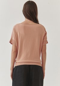 Short-sleeve, loose-fitting top in soft pink material, with a wide neckline, ribbed cuffs, and hem, paired with black lightweight trousers.