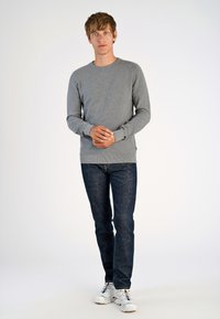 Maglione grigio a maglia con scollo rotondo, maniche lunghe e polsini a coste. Abbinato a jeans denim blu scuro e sneakers bianche.