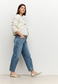 Fehér, bordázott kardigán arany gombokkal, világoskék, laza szabású farmerrel párosítva. Fémes arany balerinacipővel kiegészítve. Egyszerű, hétköznapi öltözék.