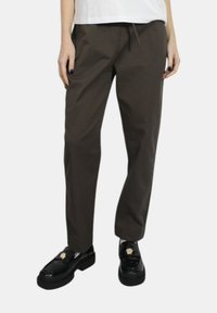 Pantaloni marroni, leggeri, a gamba dritta con vita elastica e cordoncino. Abbinati a mocassini neri, spessi, con un accento dorato.