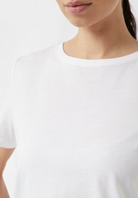 Biały t-shirt z okrągłym dekoltem, wykonany z miękkiego materiału, z krótkimi rękawami, o gładkiej fakturze i prostym, minimalistycznym designie bez wzorów.