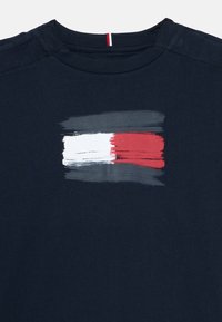 Mörkblå bomull t-shirt med ett målat horisontellt penseldrag i grått, vitt och rött. Rund hals med röd detalj på baksidan.