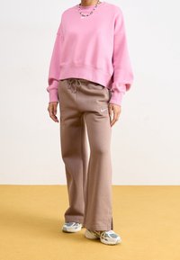 Rosa kortärmad sweatshirt och beige sweatpants med dragsko. Sweatpants har en liten logo. Skor har ljusblå och grå accenter.