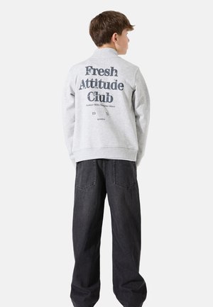 Grijze sweatshirt met de tekst "Fresh Attitude Club" en een graphic op de achterkant, gecombineerd met donkerdenim jeans met grote zakken.