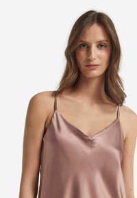 Satin camisole i dämpad rosafärg med tunna axelband och V-ringning. Slät textur med en subtil lyster. Inga ytterligare mönster eller dekorationer.