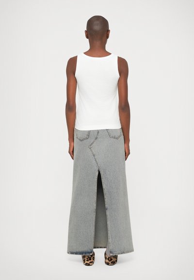 Szürke farmer maxi szoknya elöl hasítékkal, látható varrással és hátsó zsebekkel, fehér ujjatlan pólóval és leopárdmintás cipővel viselve.