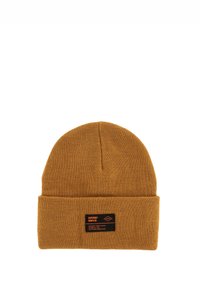 Gorro de punto en color mostaza con un borde doblado. Presenta una etiqueta de marca negra con texto blanco. Material suave y texturizado.