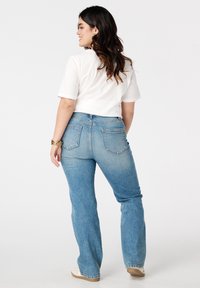 Blauwe denim flared jeans met een lichte wassing, gestikte achterzakken en een hoge taille, gecombineerd met een wit t-shirt met korte mouwen.