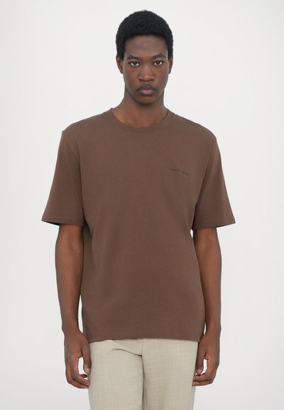 Brown cotton T-shirt with short sleeves, crew neckline, and a small light text detail on the left side. Simple, relaxed fit.
