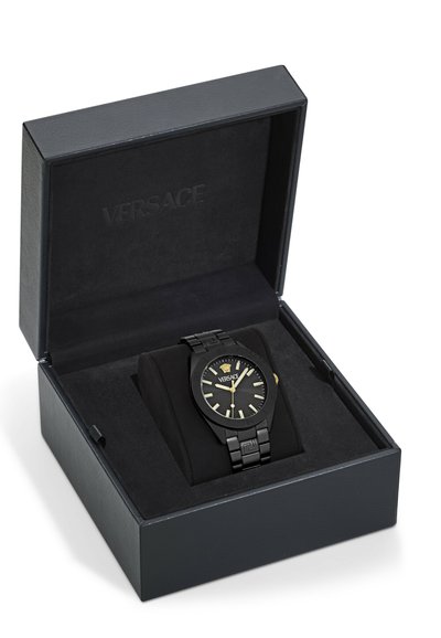Svart Versace-klocka i en vadderad displaylåda. Klockan har ett svart metallarmband, svart urtavla, guld accenter och ingraverade detaljer.