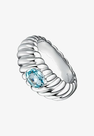 Anillo de plata con un diseño estriado, con una gema ovalada de color azul claro incrustada. Superficie suave y brillante con un patrón texturizado en forma de ondas.