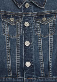 Jeansjacke mit spitzem Kragen, silbernen Druckknöpfen, zwei Brusttaschen, kontrastierenden Nähten und einer verwaschenen blauen Textur.