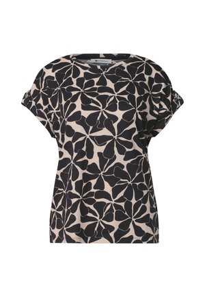 Chemise beige à manches courtes avec grand motif abstrait de feuilles noires et manches retroussées maintenues par des boutons.