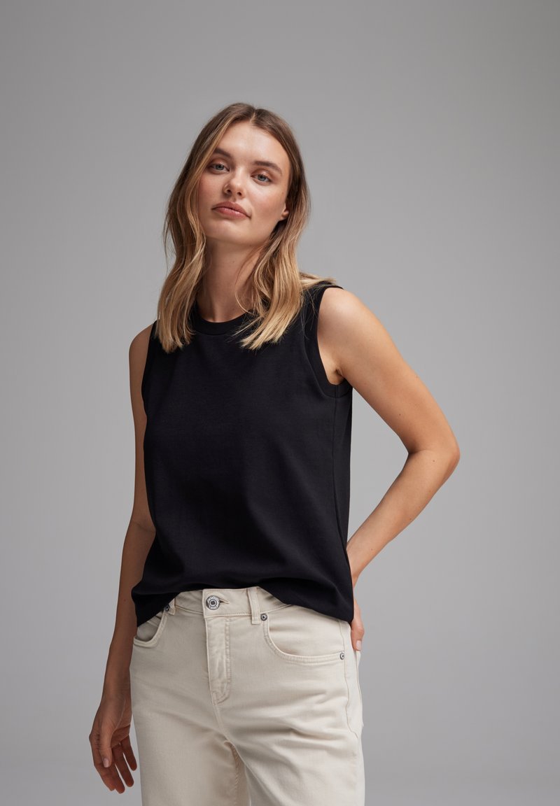 Top senza maniche nero realizzato in tessuto morbido, con scollatura a girocollo e vestibilità comoda, abbinato a jeans chiari. Dettagli di design semplici.