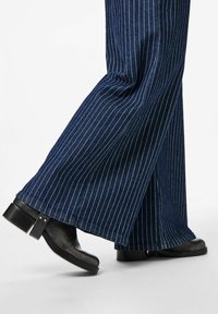 Plati legi, tumši zili denim bikses ar baltām svītrām un melni platformas potītes zābaki ar sudraba sprādzi un teksturētu virsmu.