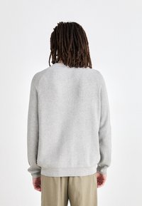 Grå stickad tröja med en åtsittande nederkant och ribbad textur, med raglanärmar och en enkel, ren design.