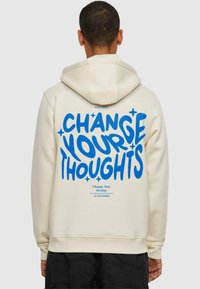 Cream-colored hoodie featuring a large blue graphic text on the back that reads "CHANGE YOUR THOUGHTS," with additional smaller text below.