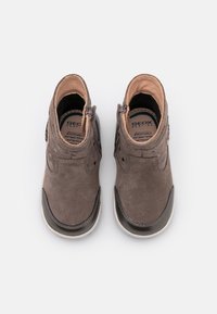 Pár šedých semišových bot pro malé děti se bočními zipy, černými špičkami a prodyšnými antibakteriálními vložkami, zobrazené zeshora na bílém pozadí.