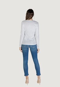 Maglietta bianca a maniche lunghe abbinata a jeans blu. La maglietta ha una texture morbida e i jeans presentano un taglio classico con tasche posteriori. Focus chiaro sui capi d'abbigliamento.