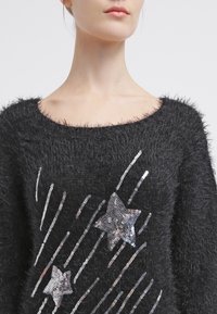 Suéter negro de lana suave con un escote ancho, adornado con estrellas de lentejuelas plateadas y franjas diagonales de lentejuelas que crean un diseño texturizado.