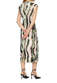 Ärmelloses Kleid mit einem wellenförmigen Muster in Grün, Schwarz und Pink. Verfügt über seitliche Schlitze und ein mittellanges Design. Getragen mit schwarzen High Heels.