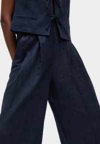 Ensemble en lin bleu marine comprenant un top court avec un détail de nœud et un pantalon à jambes larges avec des plis, mettant en avant une texture douce et une coupe ajustée.