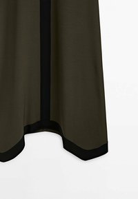 Vêtement vert olive avec une bordure noire, doté d'une texture lisse, d'un ourlet incurvé et d'une bande noire verticale au centre.