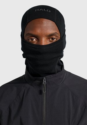 Person wearing a black balaclava with "HALO" on the forehead and a black zip-up jacket against a plain light background.