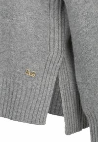 Grauer Strickpullover mit gerippter Textur und seitlichen Schlitzen. Verfügt über ein kleines goldenes Logo-Tag am Saum, das das Design aufwertet.