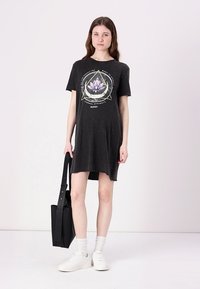 Black jersey t-shirt dress with a graphic lotus design and text. Short sleeves, round neckline, and straight cut. Styled with white sneakers.