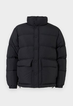Schwarze Daunenjacke mit hohem Kragen, sichtbaren Nähten, Druckknöpfen und zwei Fronttaschen; sie hat eine gesteppten Textur und eine lockere Passform.