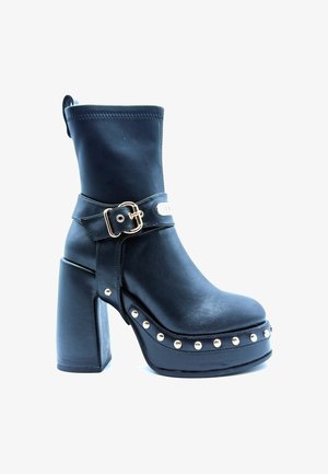 Stivale alla caviglia in pelle nera con tacco a blocco alto, dotato di una cinghia con fibbia, accenti in hardware dorato e dettagli con borchie lungo la suola.