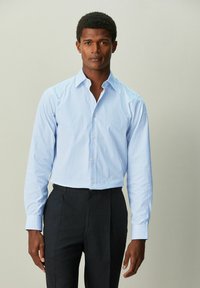 Camisa de vestir con rayas azul claro, cuello puntiagudo, mangas largas, botones marrones y diseño ajustado, combinada con pantalones oscuros.