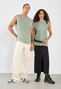 Grønne ærmeløse skjorter, kremfargede baggy bukser, svart maxiskjørt med sideutslett, svarte støvler og joggesko med teal-detaler.