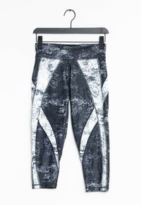 Legíny s černo-bílým vzorem, které mají texturovaný design, s kontrastními bílými akcenty a širokým pasem, zavěšené na háčku.