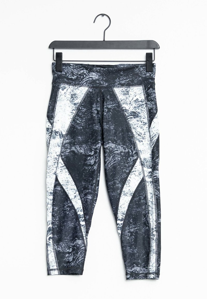 Legíny s černo-bílým vzorem, které mají texturovaný design, s kontrastními bílými akcenty a širokým pasem, zavěšené na háčku.