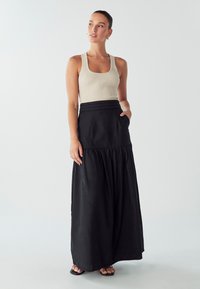 Gonna maxi nera con orlo arricciato, vita elasticizzata e tasche laterali, abbinata a una canotta a coste di un beige chiaro. Tessuto morbido al tatto.