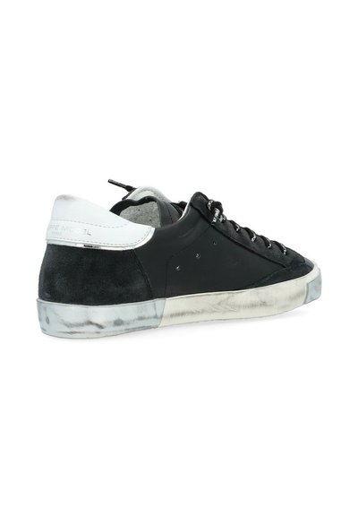 Baskets noires en daim et cuir, avec des accents blancs au niveau du talon, des lacets plats et une semelle en caoutchouc texturée. Présente un design perforé.