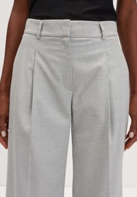 Pantaloni su misura grigio chiaro in tessuto texturizzato, con vita piatta, doppie pince, passanti per la cintura e tasche laterali.