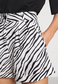 Short taille haute rayé zèbre noir et blanc avec plis devant et fermeture par bouton, porté avec un top noir.