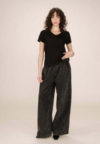 T-shirt in cotone nero con scollatura a V, abbinato a pantaloni in denim grigio scuro, larghi e con vita alta. I pantaloni sono dotati di una vita elastica e gambe larghe.