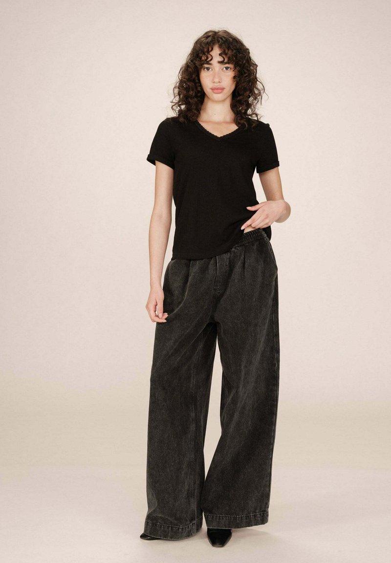 T-shirt in cotone nero con scollatura a V, abbinato a pantaloni in denim grigio scuro, larghi e con vita alta. I pantaloni sono dotati di una vita elastica e gambe larghe.