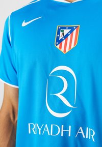 Blue sports jersey featuring white accents, Nike logo, Atlético Madrid badge, and "RIYADH AIR" in white text. Smooth, breathable fabric.