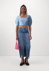 Top court bleu clair avec manches bouffantes, jupe en denim bleu taille haute avec fente à l'avant, petit sac à main rose et chaussures à plateforme noires.